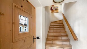 Una puerta de madera con un ventanal, una escalera con barandillas de madera y un estante de pared con objetos.