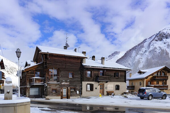 Un edificio de madera con balcones, techo nevado y montañas al fondo.