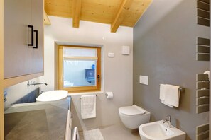 Un baño moderno con un ventanal grande, un lavabo, un inodoro y un bidé.