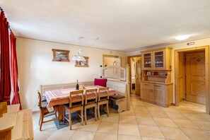 Un comedor con mesa dispuesta para cuatro personas, sillas de madera, un banco y un mueble con puertas de vidrio.