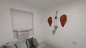 A bedroom with a bed, pillows, a window with blinds, and two wall-mounted hats.