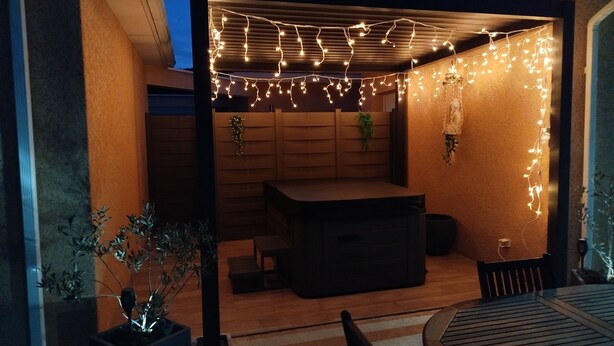 Un espacio de estar al aire libre cubierto con luces colgantes, una mesa de madera y sillas.
