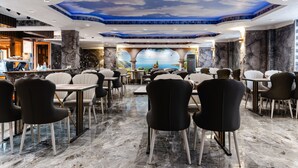 Un ristorante con pavimenti in marmo, sedie nere e bianche e un affresco al soffitto raffigurante cielo e paesaggio.