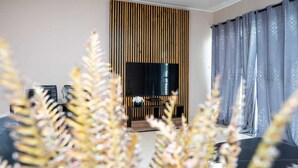 Una sala de estar moderna con un televisor de pantalla plana grande, un muro de listones de madera y una cortina gris estampada.