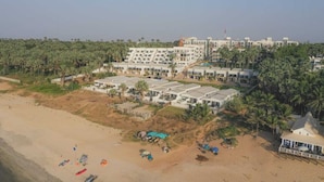 Un hotel frente al mar con varias edificaciones, una zona de playa y palmeras.