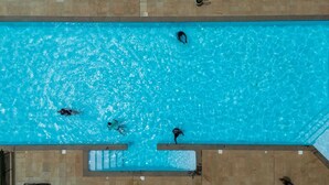 Vista aérea de una piscina rectangular con agua azul cristalina, rodeada por una zona de solárium con baldosas.