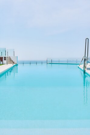 A clear blue pool with a glass barrier, steps leading into the water, and a view of the ocean.