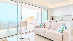 Een moderne woonkamer met een bank, een glazen salontafel en uitzicht op het strand door grote schuifpuien.