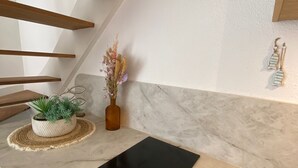 A kitchen with a black induction cooktop, wooden beams, a marble backsplash, and a small potted plant. - Waterfront apartment (sea view) (Concarneau)