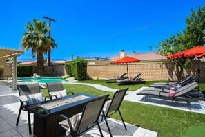 A backyard with a pool, lounge chairs, and a table with chairs.