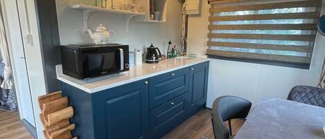 A modern kitchen with blue cabinets, a microwave, and a coffee maker. There is a wooden rack and a dining table with chairs.