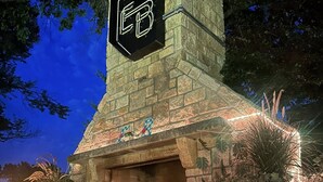 Ein Kamin aus Stein mit einem sechseckigen Logo, umgeben von Topfpflanzen und einer Steinsäule.