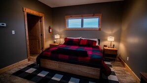 A bedroom with a bed, two bedside tables, a window, and a door. - King Cabin Room Lark Spur (Maple Hill)