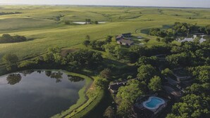 Vue aérienne d’une propriété comprenant un grand étang, une piscine et un bâtiment entouré d’une végétation luxuriante.