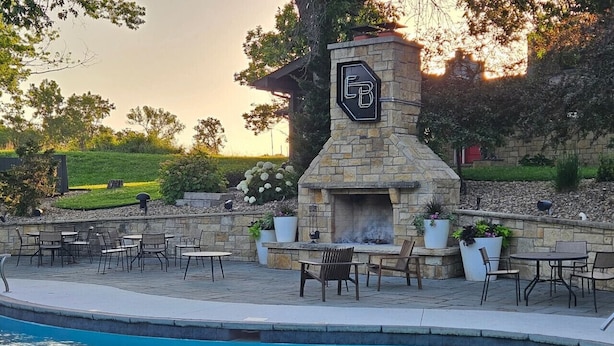 A poolside area with a stone fireplace, outdoor seating, and a view of the surrounding landscape.