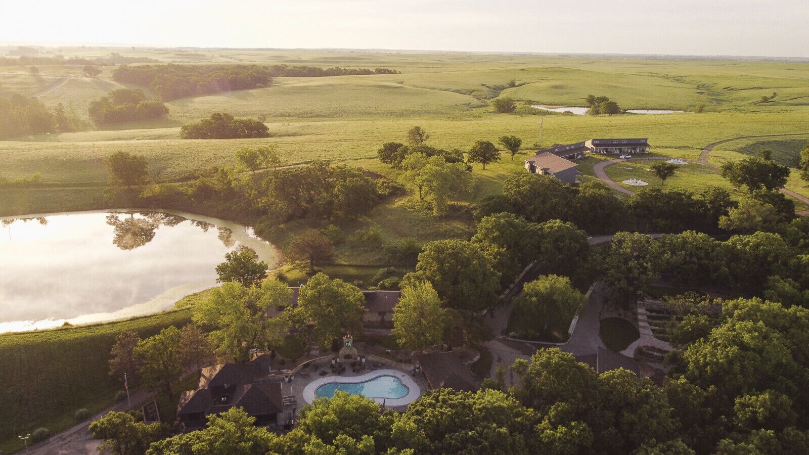 An aerial view of a property with a swimming pool, surrounded by lush greenery and a lake.
