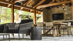 An outdoor patio with wooden beams, stone walls, a stone fireplace, and wicker furniture. - King Cabin Room Kansa (Maple Hill)