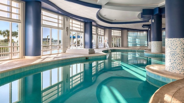 A large indoor swimming pool with clear blue water, surrounded by large windows and blue pillars. - 1BD/Daytona - Condo w/Wide Open Ocean F U N! (Daytona Beach)