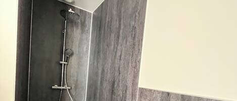 A modern bathroom with a shower, dark tiled walls, and a white countertop.