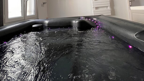 A room with a hot tub, a mounted TV, and a window with blinds.