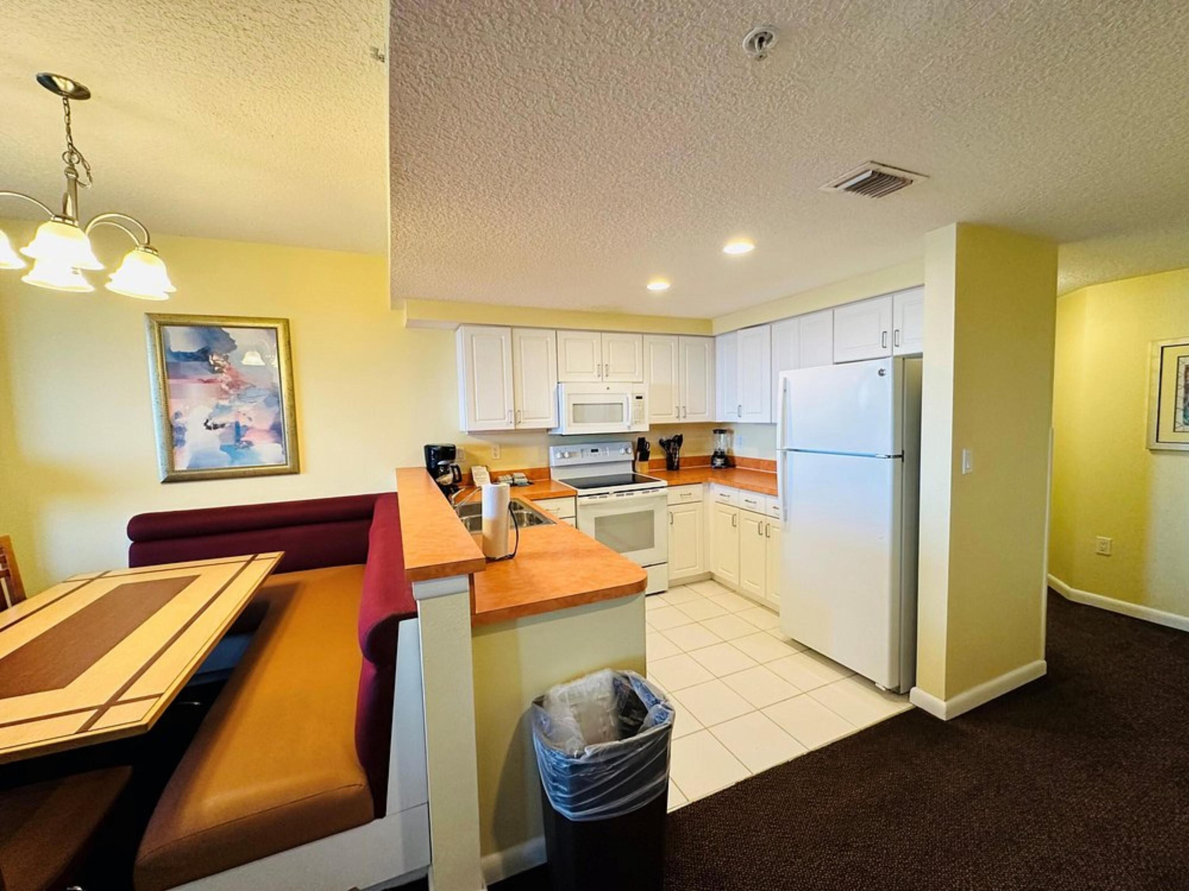 A compact kitchen with white cabinets, a microwave, stove, and a refrigerator. There is a dining area with a bench and a table.