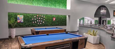 A pool table area with two tables, a green wall with a fire extinguisher, and a bar area with a coffee machine.