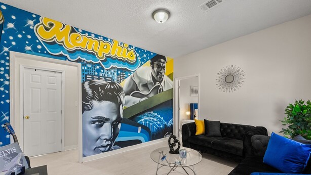 A living room with a mural, a black sofa, a glass coffee table, and a door.