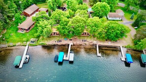 An aerial view of a lakeside property with docked boats, a small dock, and several buildings surrounded by lush greenery.