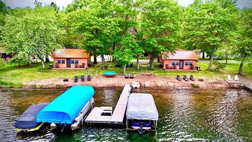 Un chalet au bord du lac, avec un quai, un bateau à moteur abrité et un petit bateau.