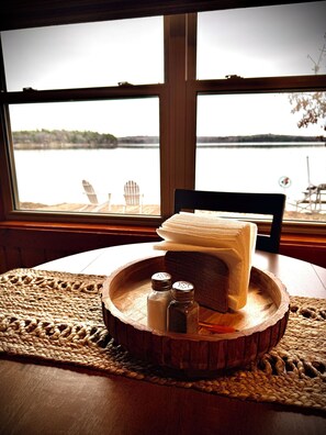 A wooden table with a woven placemat, a stack of white towels, two salt and pepper shakers, and a chair.
