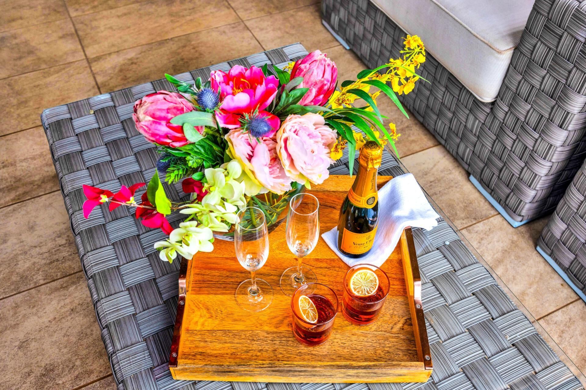 Una mesa de mimbre con un ramo de flores, una botella de champán y dos copas sobre una bandeja.
