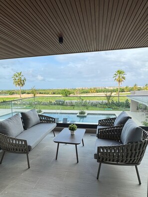 A modern outdoor seating area with a pool, overlooking a landscaped garden and distant buildings.