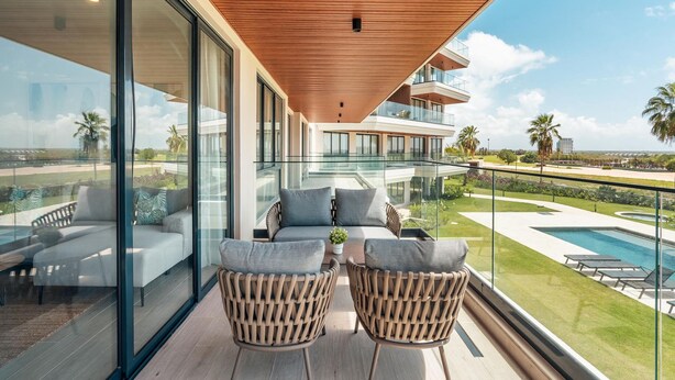 Ein moderner Balkon mit Glasgeländern, zwei Korbstühlen und Blick auf einen Pool und Grünflächen.
