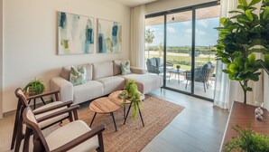 Ein modernes Wohnzimmer mit Sofa, Couchtisch und Sesseln, ein Balkon mit Landschaftsblick und abstrakte Kunst an der Wand.
