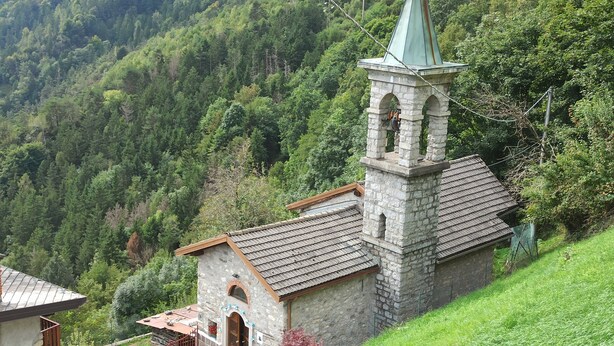 Une église en pierre dotée d’un clocher et d’une petite cloche, entourée d’une forêt verdoyante et luxuriante.