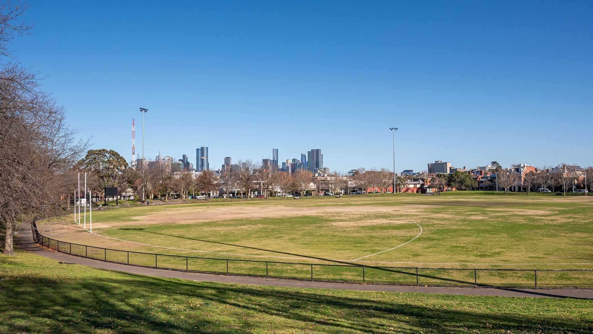 A large open grassy field with a running track, surrounded by a fence and trees.