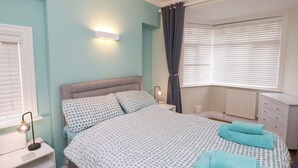 Un dormitorio con cama, mesita de noche, lámpara, ventana con persianas y radiador.