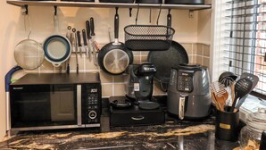 Una cocina con microondas, cafetera y diferentes ollas y sartenes en estantes.