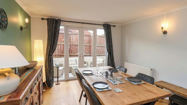 Comedor con una mesa de madera para cuatro, una lámpara y vistas a un patio exterior por un ventanal.
