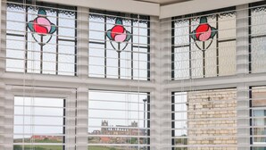 Una habitación con ventanas amplias con diseños de vitrales y vistas a un edificio histórico.