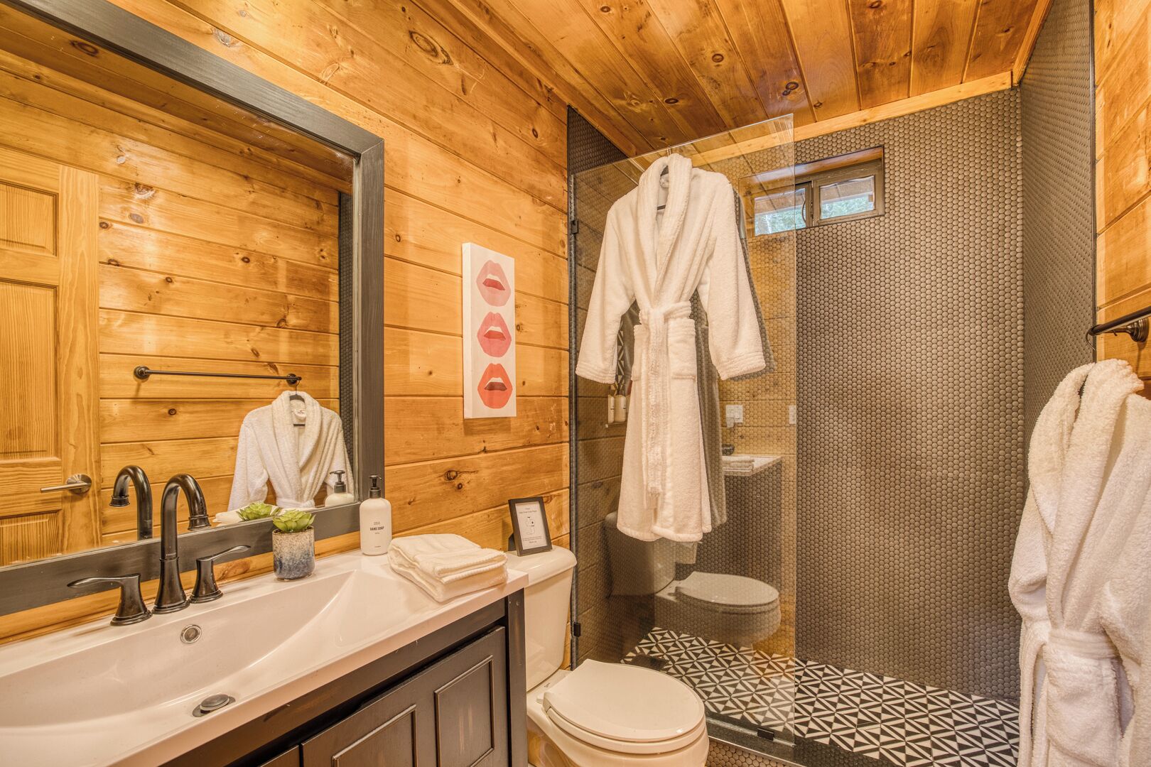 A wooden cabin bathroom with a large mirror, a sink with a faucet, a toilet, and a shower area.