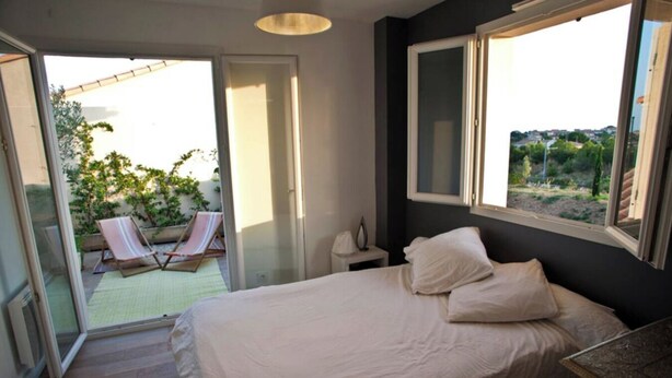 A bedroom with a bed, a nightstand, and a window with a view of the outdoors. - House with pool near Montpellier Plage July 12-August 2 (Le Crès)