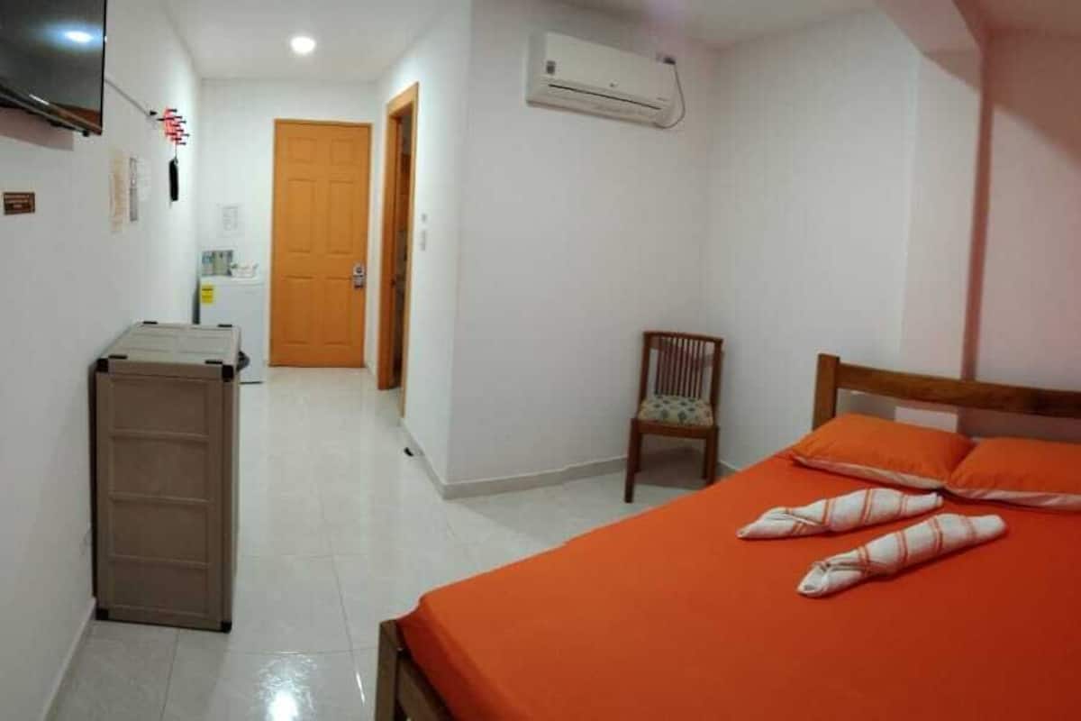 A bedroom with a bed, a chair, a wardrobe, and an air conditioning unit.