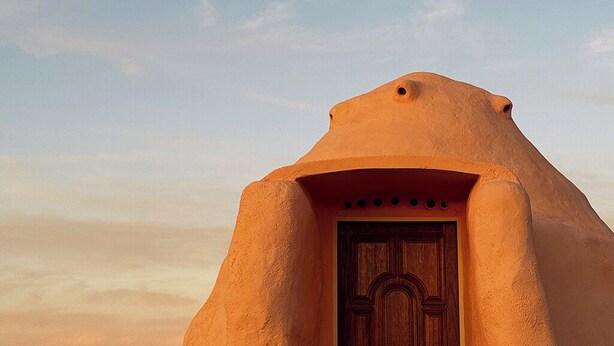 Un edificio tradicional de adobe con una puerta de madera y un ventanal pequeño.