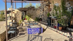 Un patio al aire libre con paredes de piedra, una mesa con mosaicos y sillas de metal.