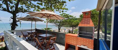 A balcony with outdoor seating, a barbecue grill, and a view of the beach.