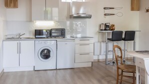 Une cuisine compacte équipée d’un lave-linge, d’un four à micro-ondes et d’une machine à café. Elle comprend deux chaises et une table.
