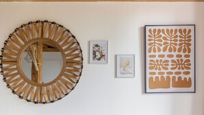Un mur orné d’un grand miroir rond, de deux reproductions botaniques encadrées et d’une œuvre d’art abstraite encadrée.