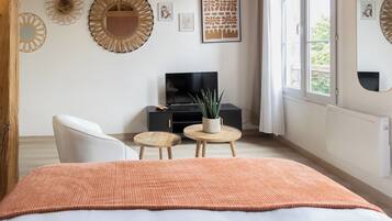 A bedroom with a bed, a TV, two small round tables, a potted plant, and decorative wall art.