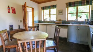 Une cuisine avec des meubles de rangement en bois, une table à manger avec des chaises, un lave-vaisselle et une fenêtre avec des rideaux.